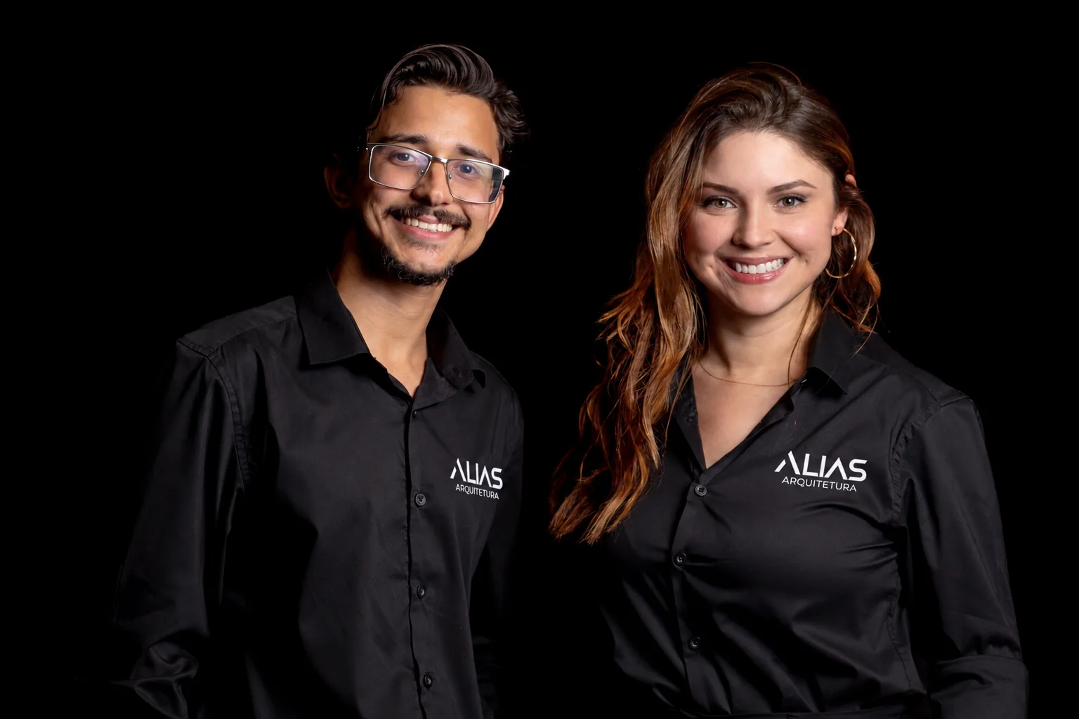Retrato da equipe da Alias Arquitetura: duas pessoas de camisa preta com o logotipo da marca, sobre fundo escuro