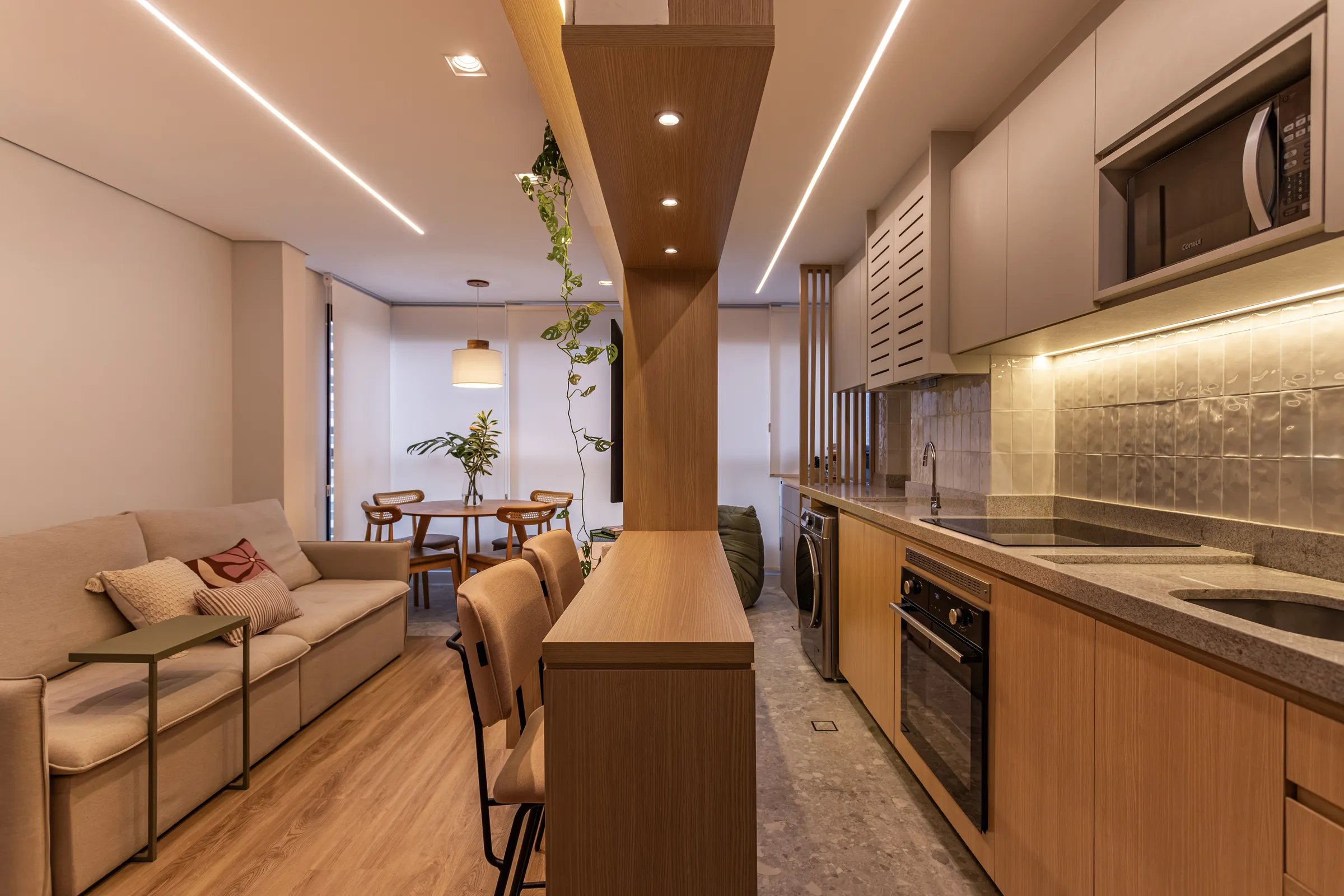 Sala de estar integrada à cozinha com marcenaria em madeira clara, iluminação em fita de LED e mesa de jantar ao fundo