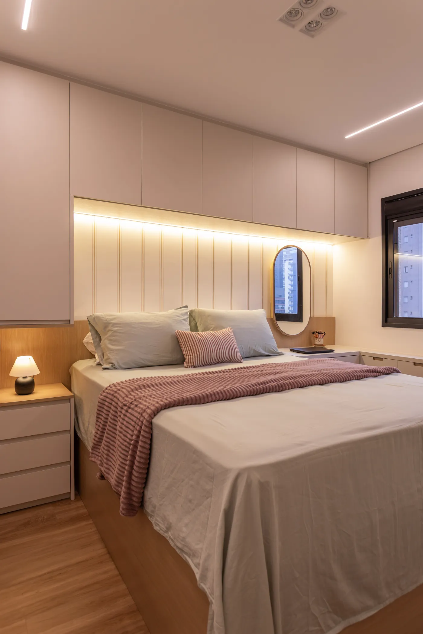 Quarto de casal com painel ripado iluminado, armário planejado e cama com roupa de cama em tons suaves