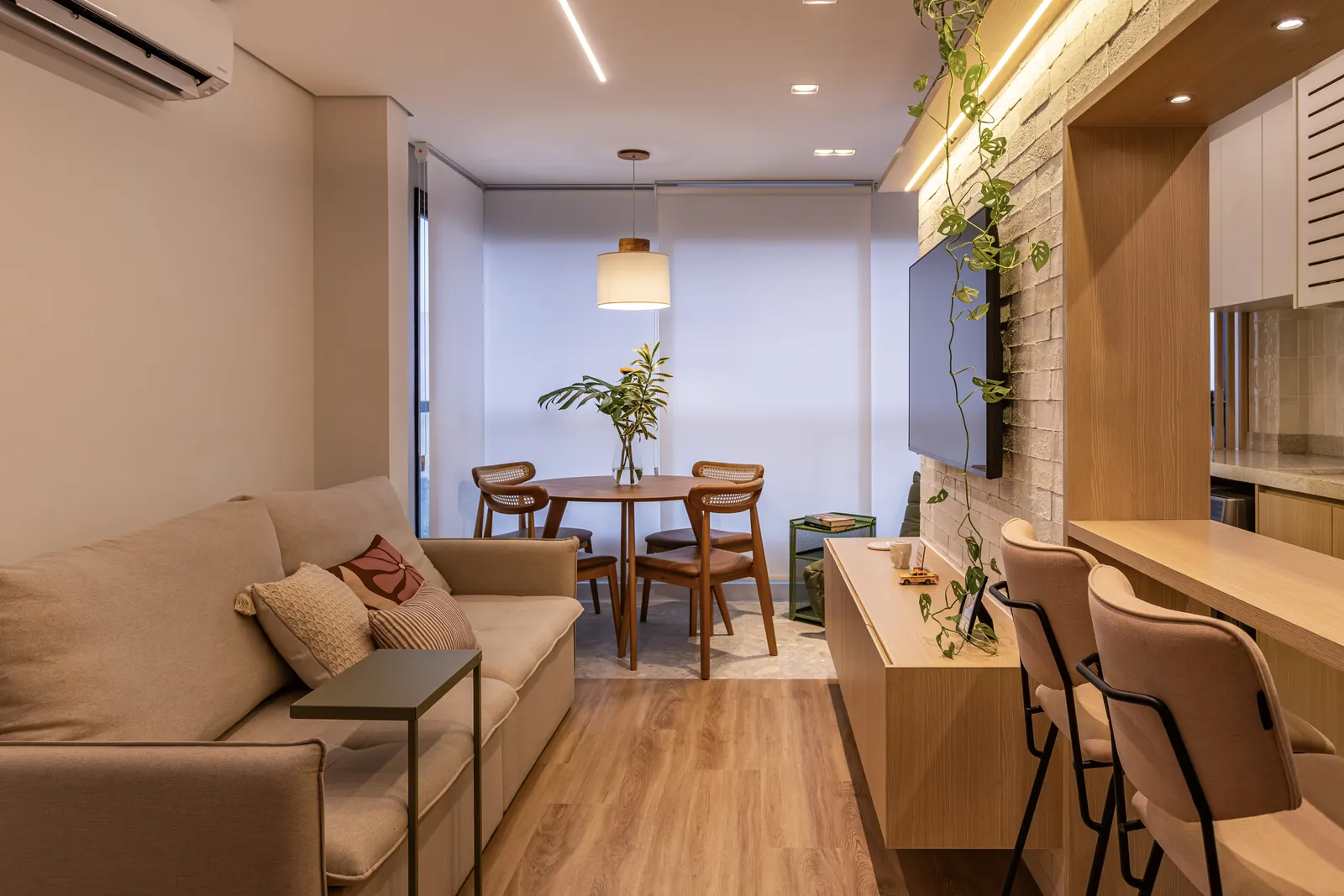 Sala de estar e jantar integradas com sofá, mesa redonda e painel de marcenaria com TV